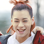 An icon of Deven. He is smiling widely, and is wearing a white shirt with a red jacket. His long redish brown hair is tied up in a top-knot.