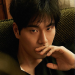 An icon of Valentyn. He is sitting on a green couch, and his left hand is covering his mouth. He has a dark and mysterious expression on his face. His black hair is neat, with bangs ending a little above his eyebrows.