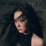 An icon of Hana. She is looking balefully towards the left, with her long black hair blowing messily around her. She is wearing a black dress.