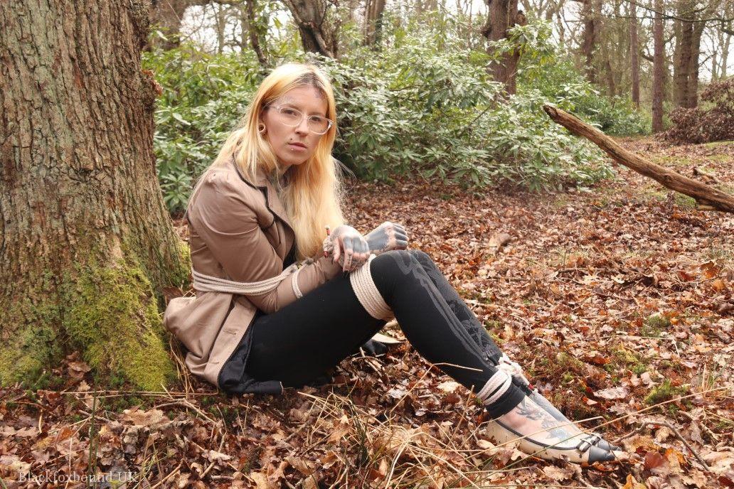 Glasses wearing woman in tied with ropes to a treed in woods with clothes on(3)