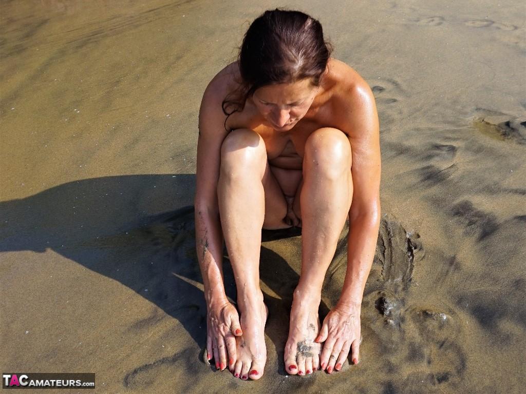 Naked older woman Diana Ananta covers her feet in beach sand at low tide(11)