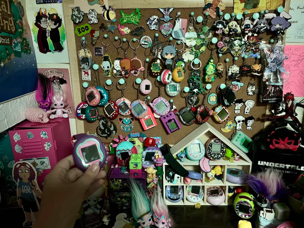 A photo of around 30 tamagotchi from across multiple eras, most on a coarkboard and the others in shelves around it.