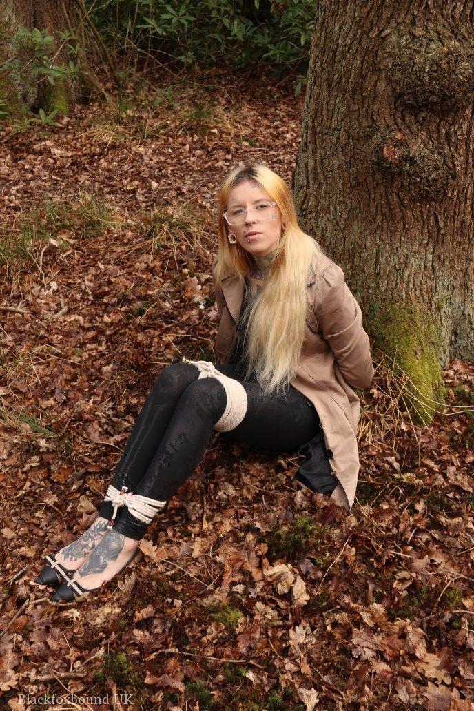 Glasses wearing woman in tied with ropes to a treed in woods with clothes on(7)