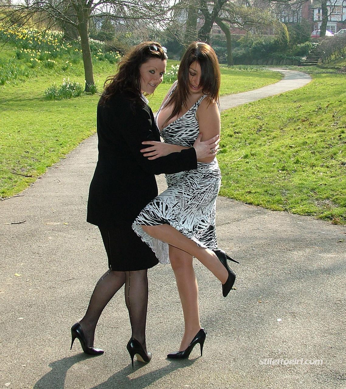 Clothed ladies hold hands while showing their spiked heels on a walking path(2)