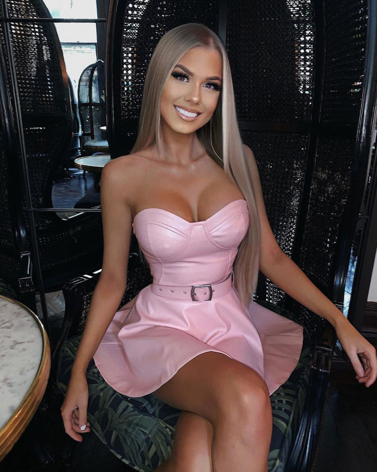 Blonde tanned girl wearing pink leather dress has cleavage on show