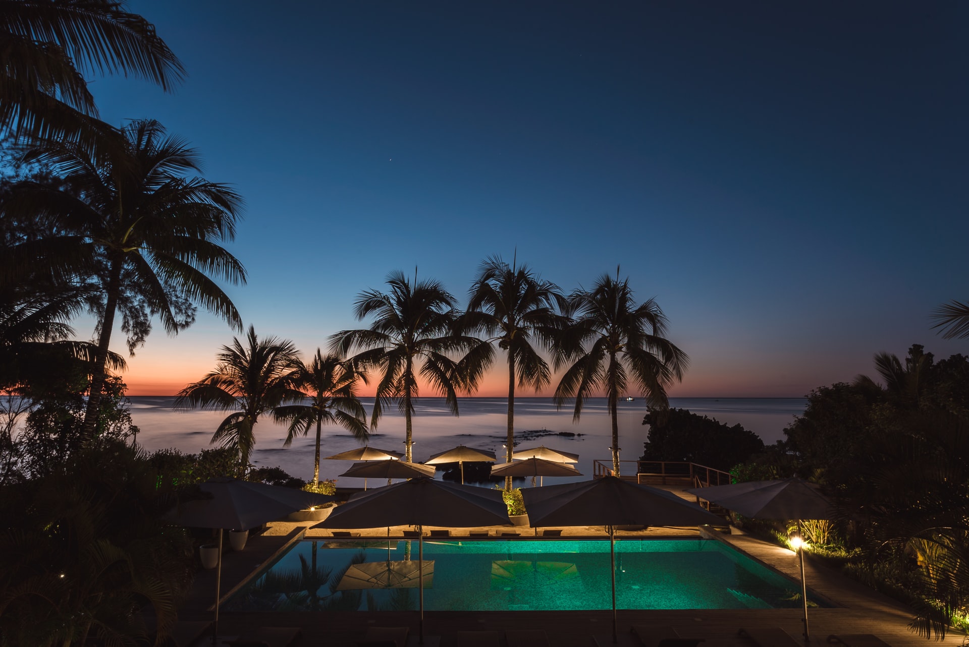 Swimming pool and parasols lit up under palm trees as dusk falls on island resort