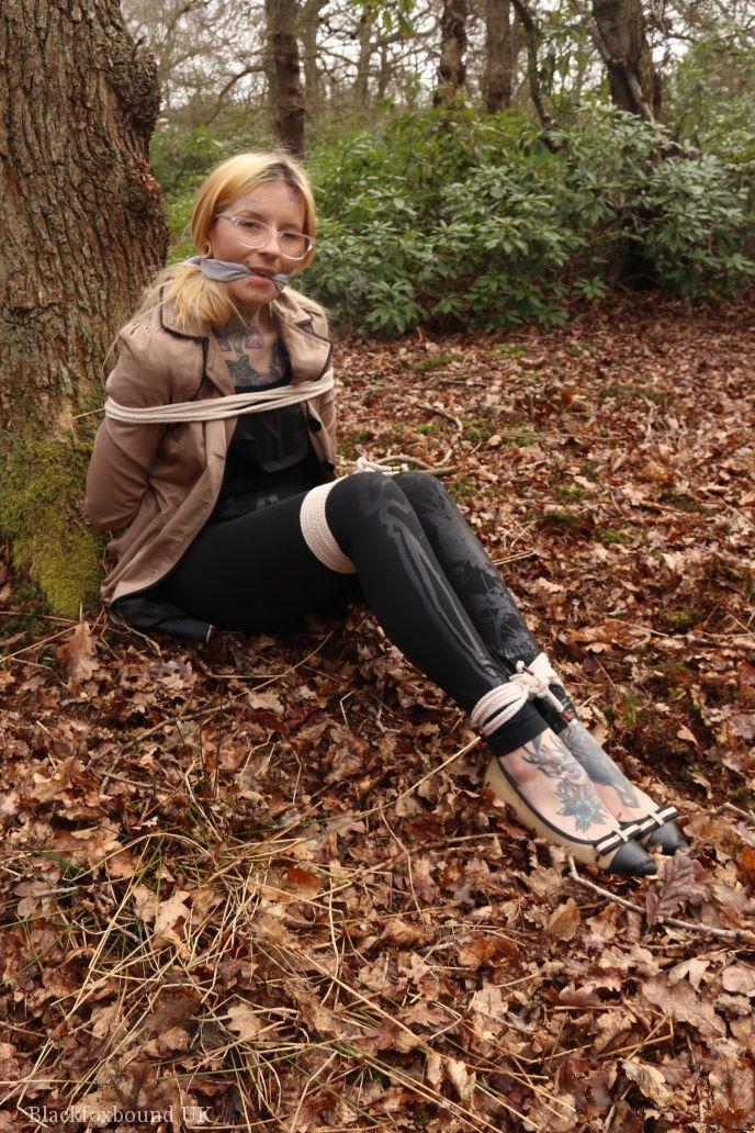 Glasses wearing woman in tied with ropes to a treed in woods with clothes on(15)