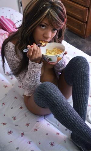 Black babe in gray socks Little Yumi flaunts her tits while eating on a bed