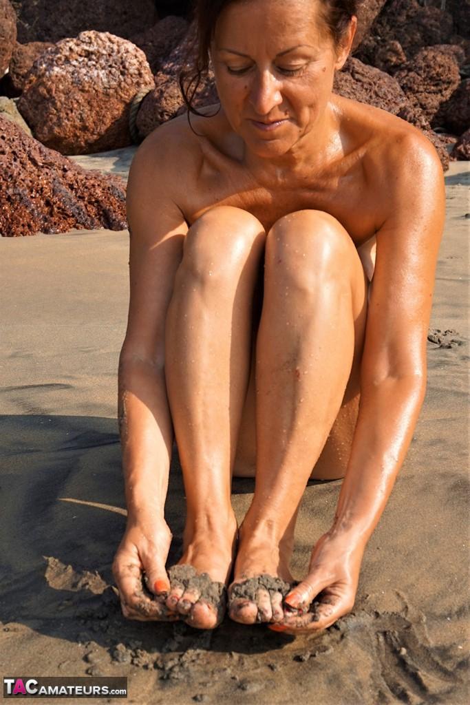 Naked older woman Diana Ananta covers her feet in beach sand at low tide(7)