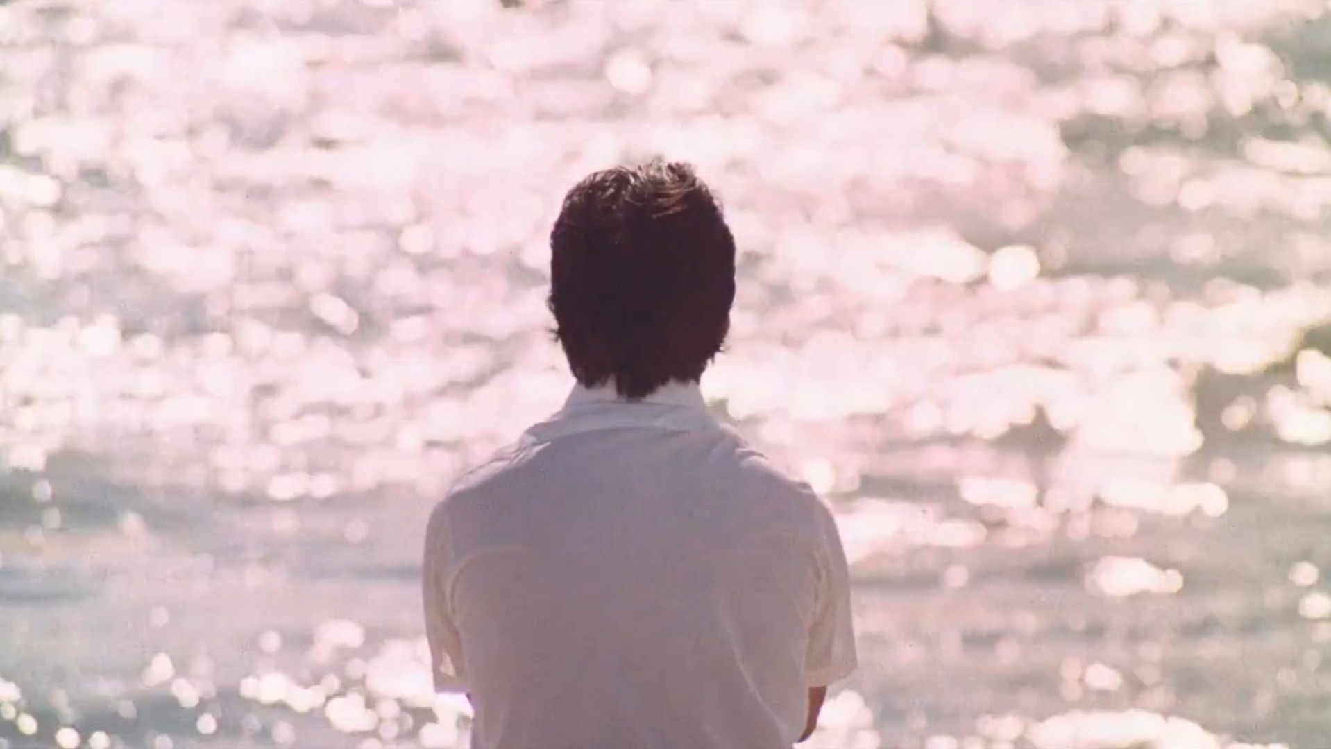 Rico Rizzo, a brown-haired man, sits in front of the ocean. His back faces us.