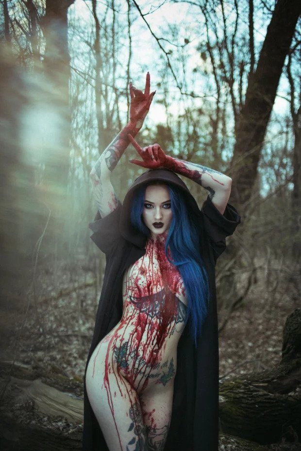 Semi-naked tattooed woman in cloak struts through forest with blood smeared on hands, neck, chest and legs