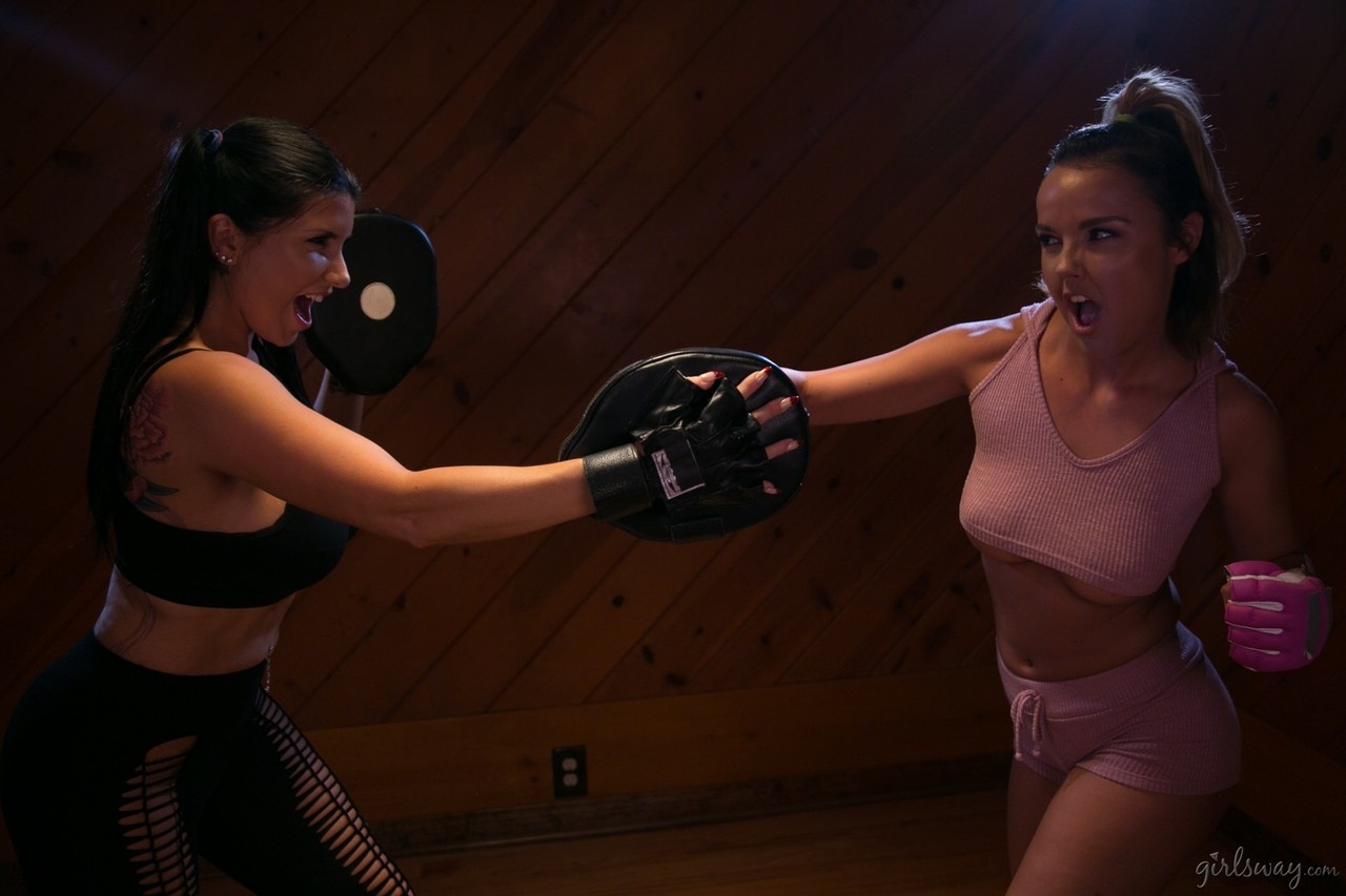 Woman in pink gym wear practices boxing with woman in black gym wear