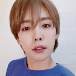An icon of Sunyoung. He is looking directly into the camera, with his lips in a heart-shaped smile. He is standing against a white wall and wearing a blue shirt.