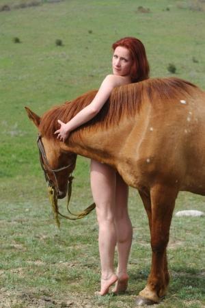 Redheaded teen Klara A poses completely naked on a huge horse outdoors