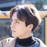 An icon of guy. He has dark brown hair, and is looking off to the left, standing in profile. He has on a black turtleneck and a brown jacket.