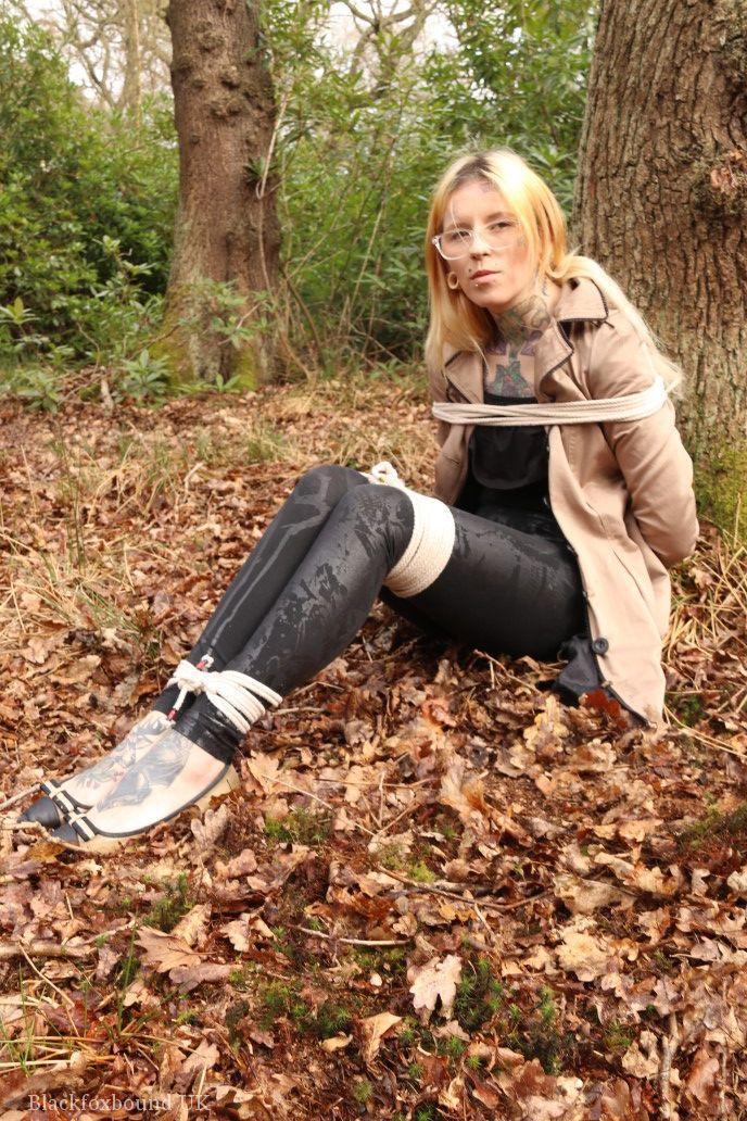 Glasses wearing woman in tied with ropes to a treed in woods with clothes on(9)