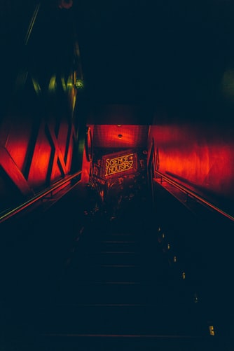 View up flight of dark stairs lit only by neon sign at top