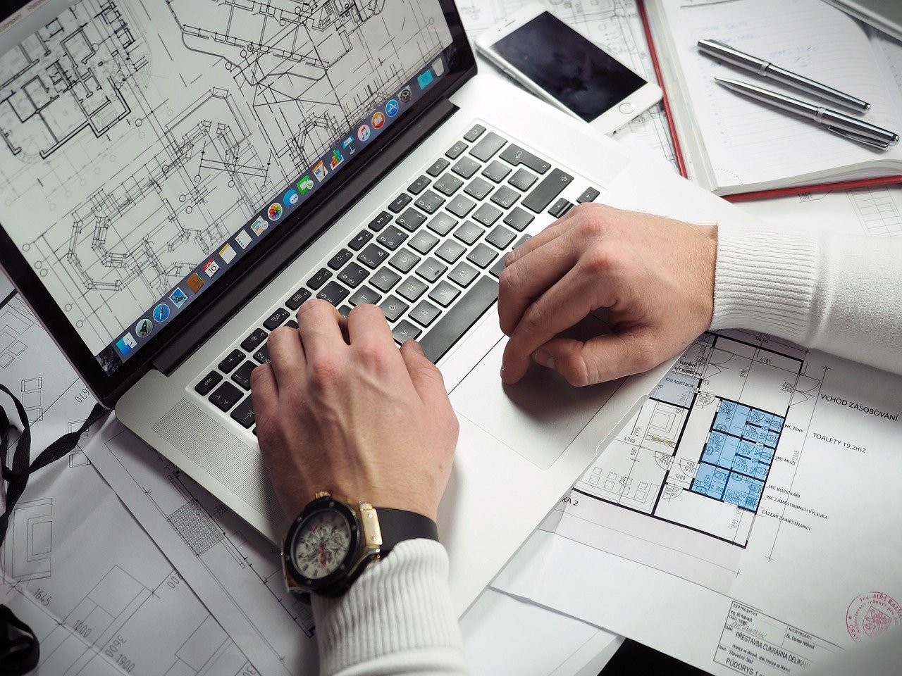 Man in cardigan works on architectural plans on laptop