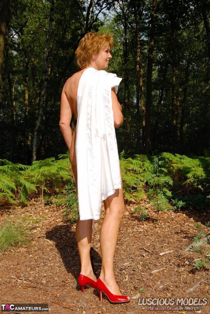 Older redhead removes a robe to stand naked in red heels while in the woods(14)