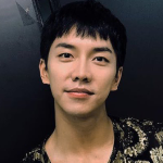 An icon of Rayner. He is looking straight at the camera and smiling a close-lipped smile. His black hair is short, with choppy bangs. He is wearing a black u-neck shirt with gold embroidery.