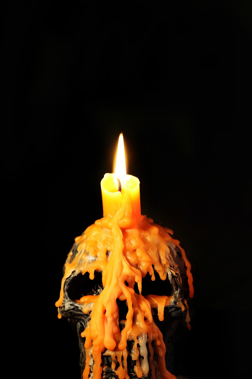 Orange candle burns atop skull covered in dried wax
