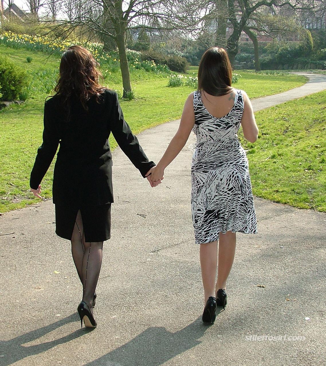 Clothed ladies hold hands while showing their spiked heels on a walking path(6)