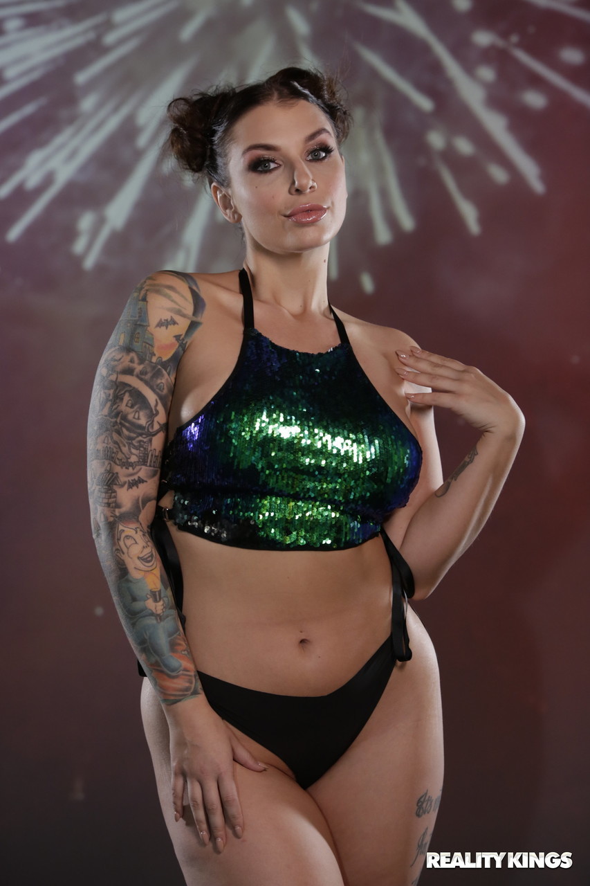 Tattooed woman with dark hair poses wearing glittery top and black underwear