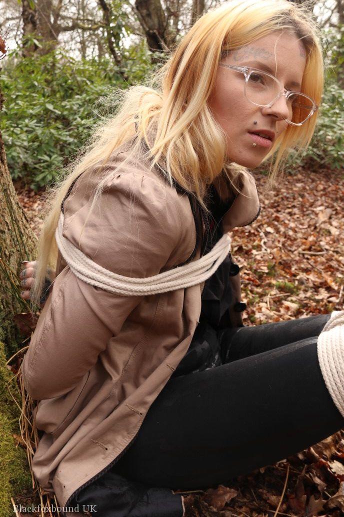 Glasses wearing woman in tied with ropes to a treed in woods with clothes on(12)