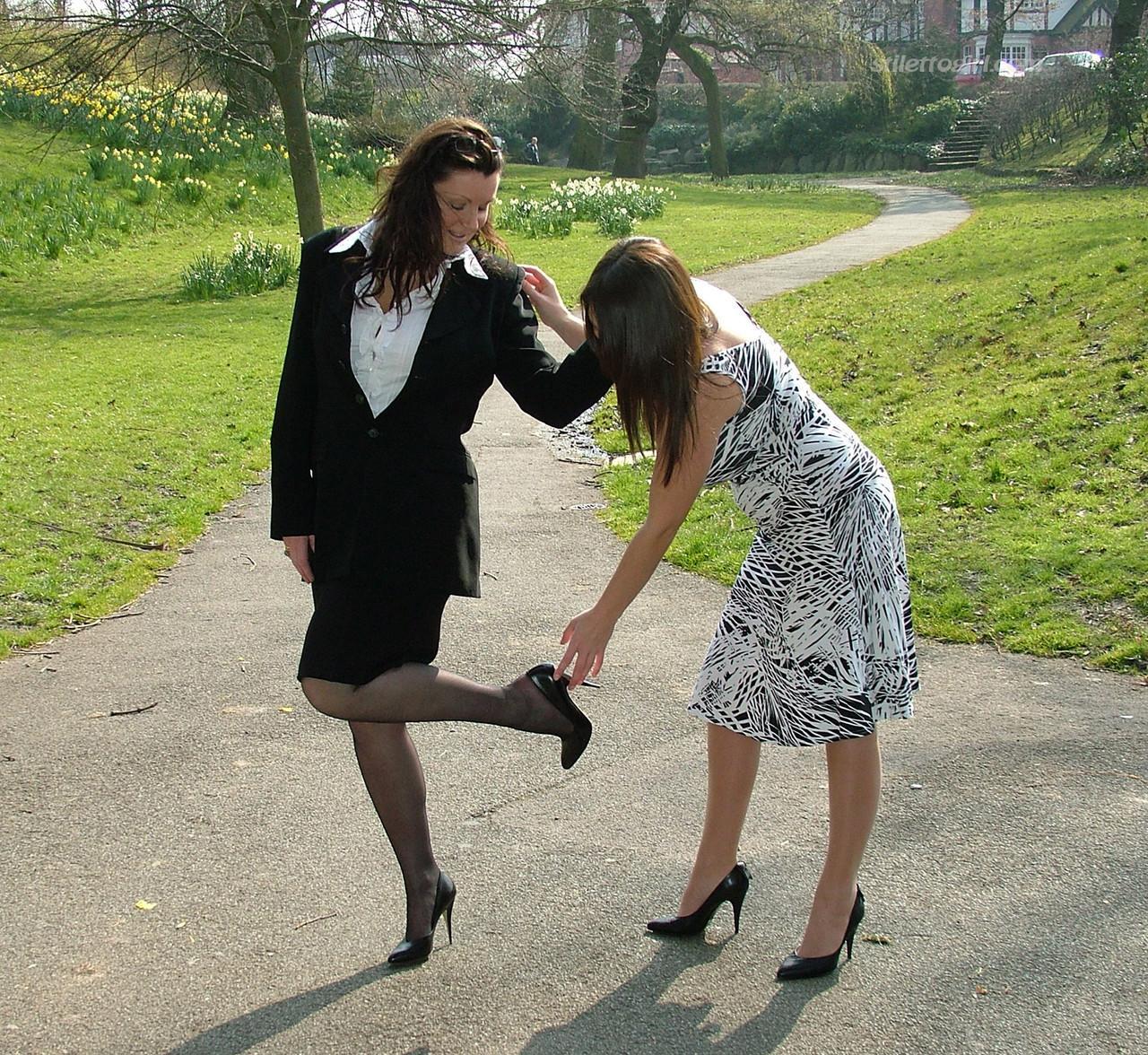 Clothed ladies hold hands while showing their spiked heels on a walking path(10)