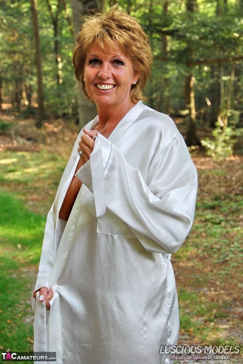 Older redhead removes a robe to stand naked in red heels while in the woods(3)