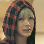An icon of Teddy. He is wearing a red and black checkered hood, with only a little bit of his silver hair showing. He is looking at the camera from the side, with an almost sour expression.