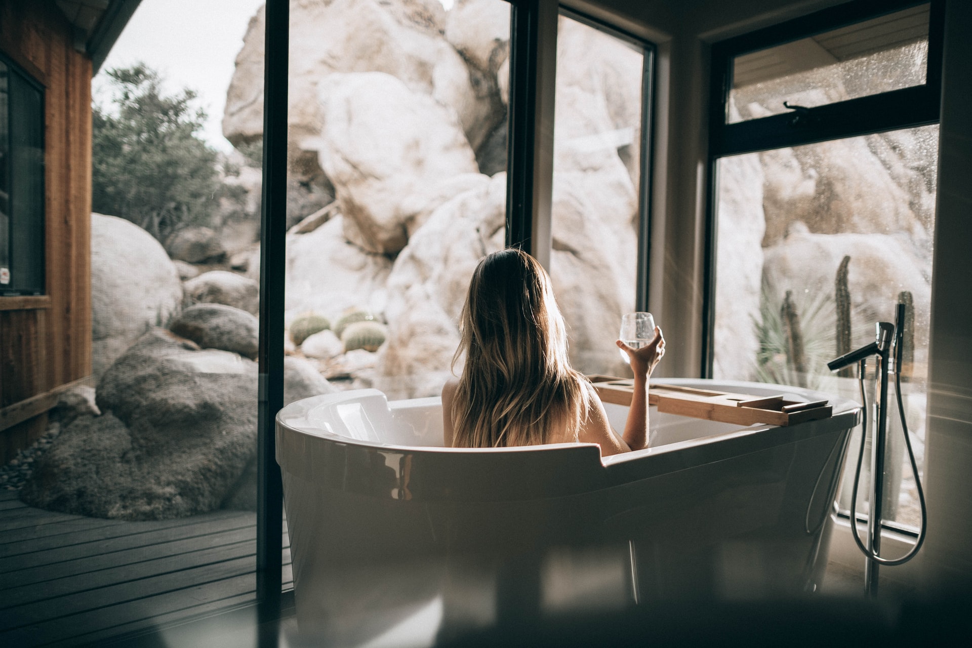 Woman takes bath with glass of wine with view of cliff face