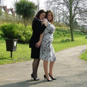 Clothed ladies hold hands while showing their spiked heels on a walking path