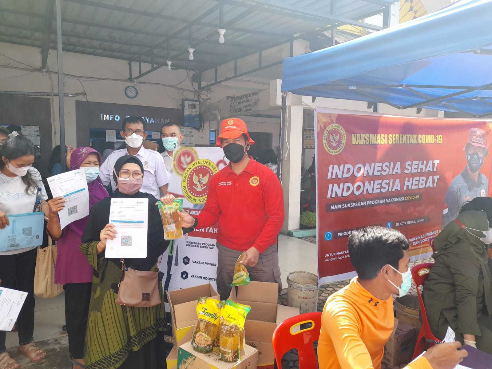 Personil Binda Sumut dan Camat Medan Perjuangan Zul Ahyudi Solin, Ap. MSi menyampaikan bantuan Minyak goreng pada peserta vaksinasi bagi 1500 masyarakat di kantor Camat Medan Perjuangan, Rabu (22/6/2022)