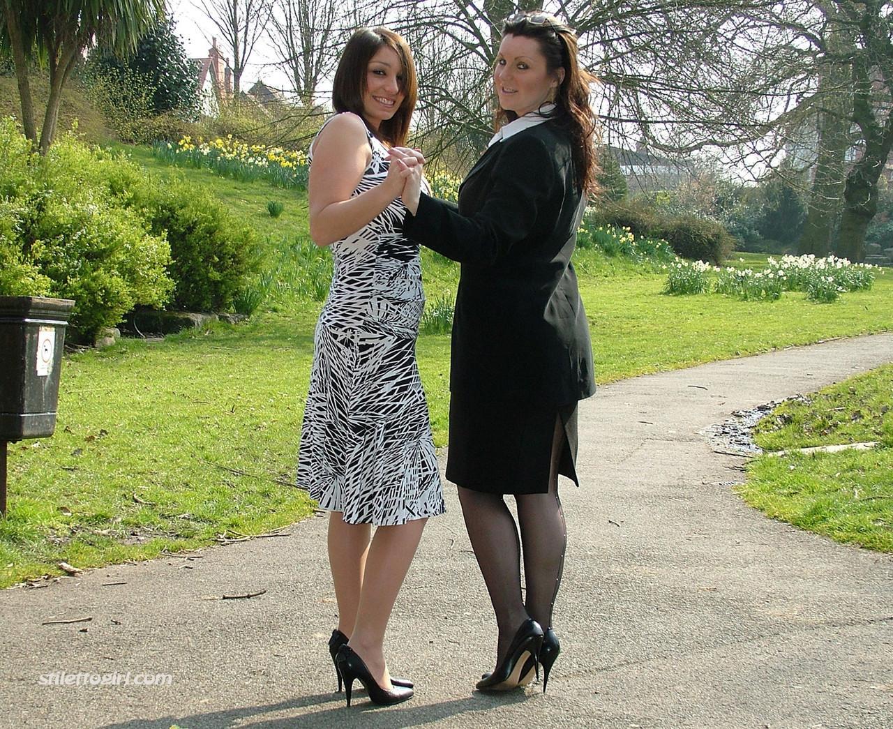 Clothed ladies hold hands while showing their spiked heels on a walking path(16)