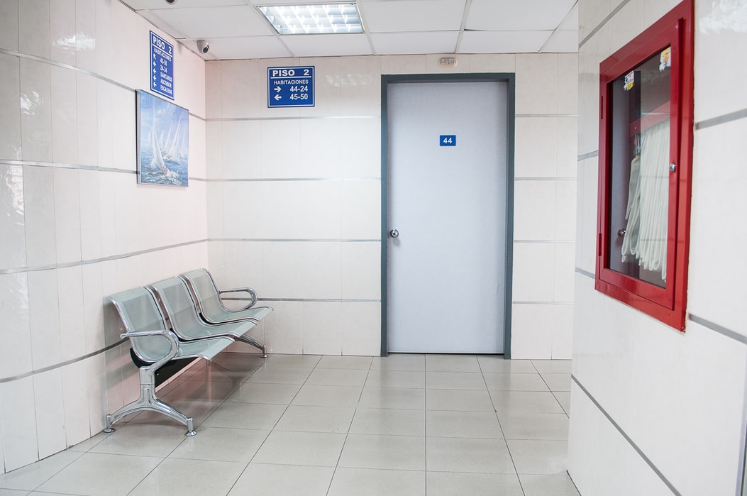 Clinical white corridor with metal bench sat beside white door