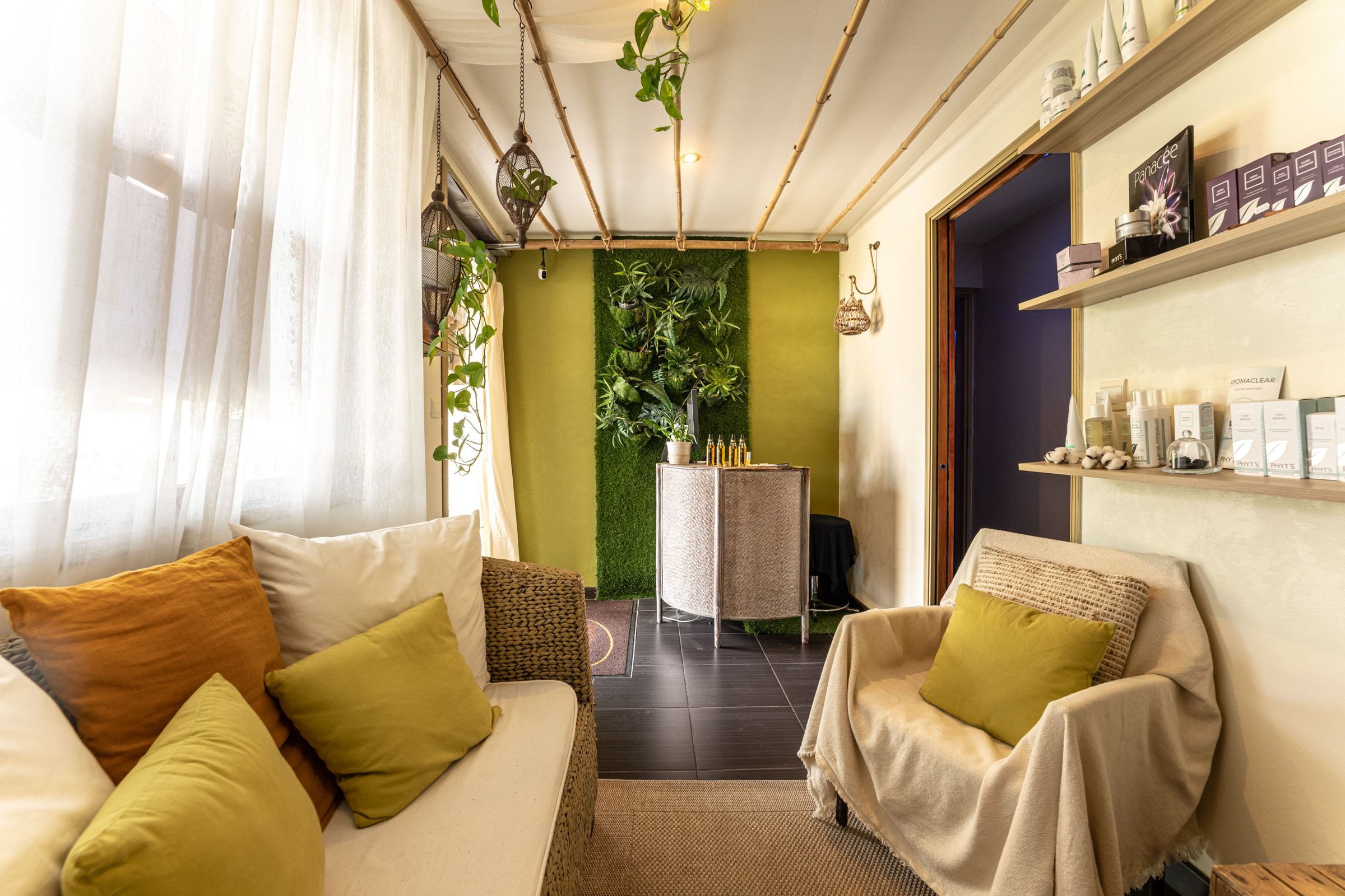 Accueil du spa, avec un canapé deux place et un autre une place, les produits son sur une étagère et il y a un mur de pelouse