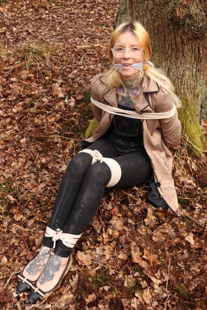 Glasses wearing woman in tied with ropes to a treed in woods with clothes on(14)