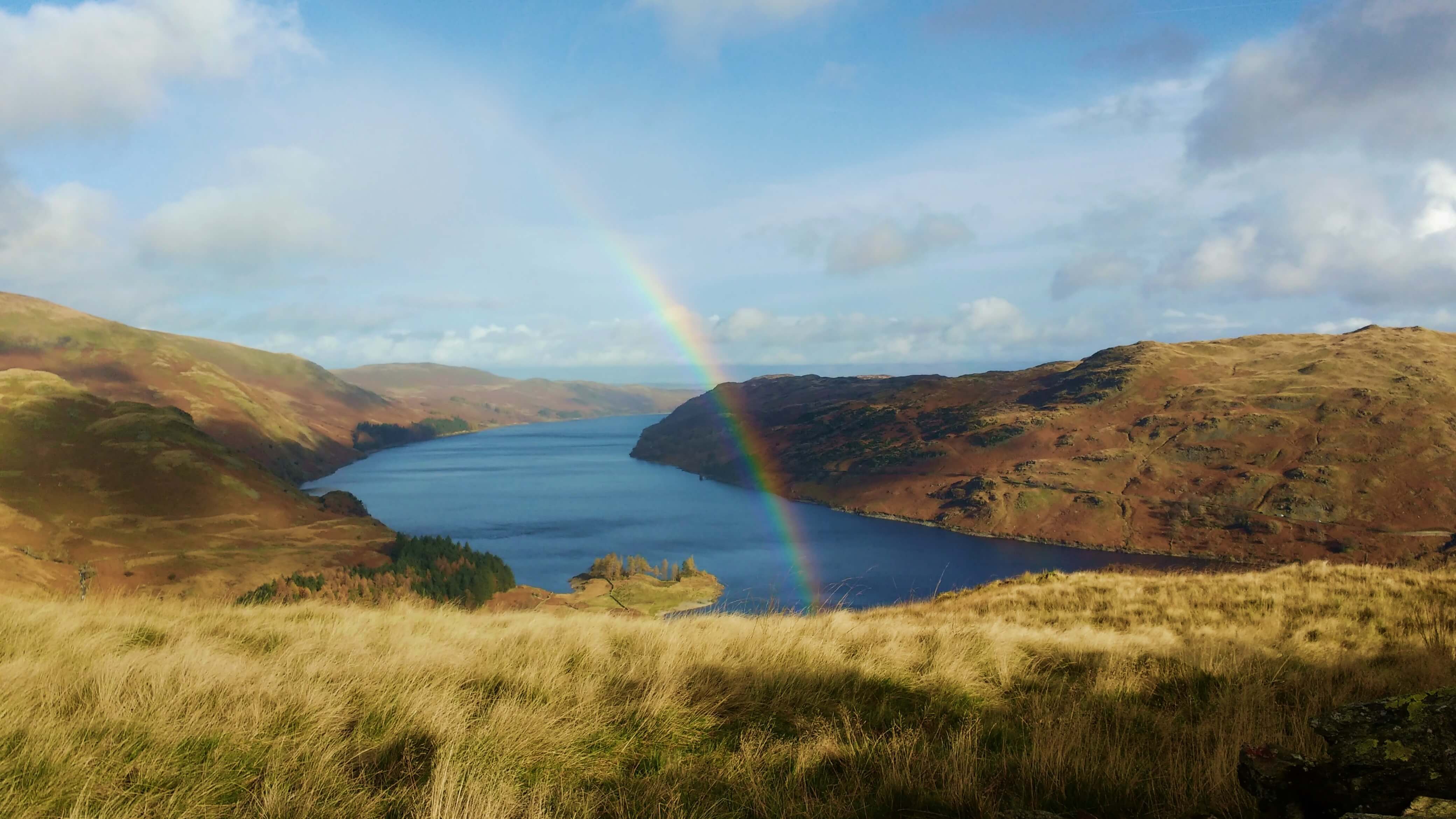 A rainbow dipping into a lake surrounded by hills