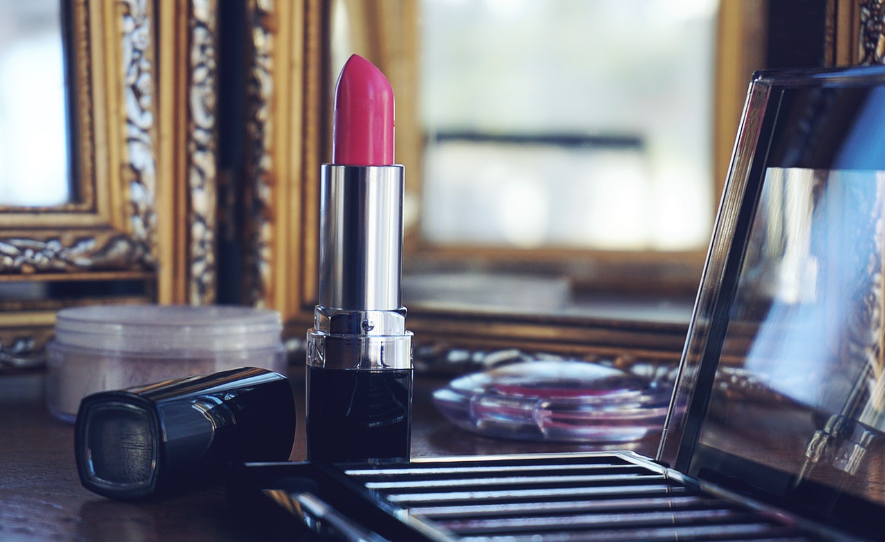 Lipstick and assorted makeup items on desk in front of mirrors