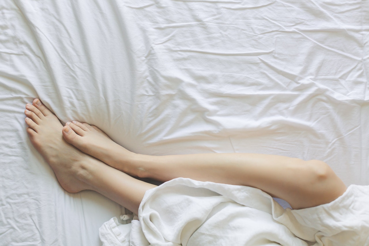 Shot of person's legs on white bedsheets