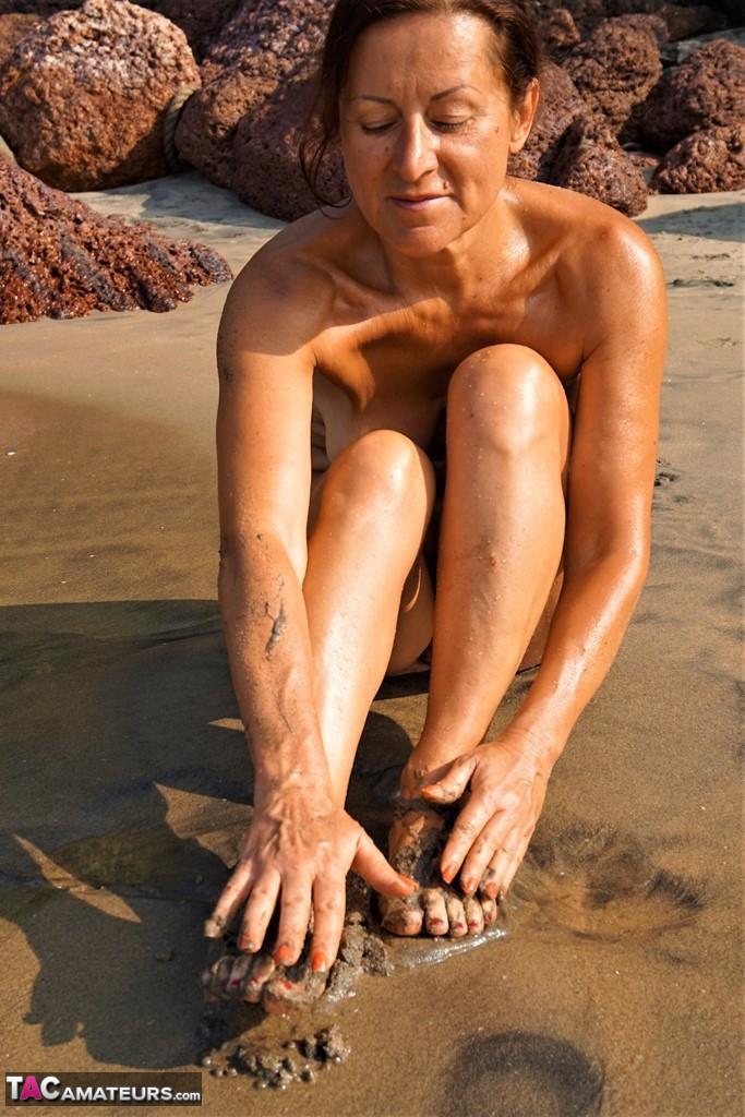 Naked older woman Diana Ananta covers her feet in beach sand at low tide(8)