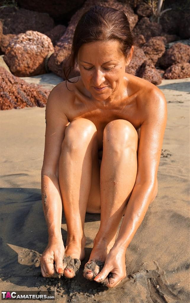 Naked older woman Diana Ananta covers her feet in beach sand at low tide(6)