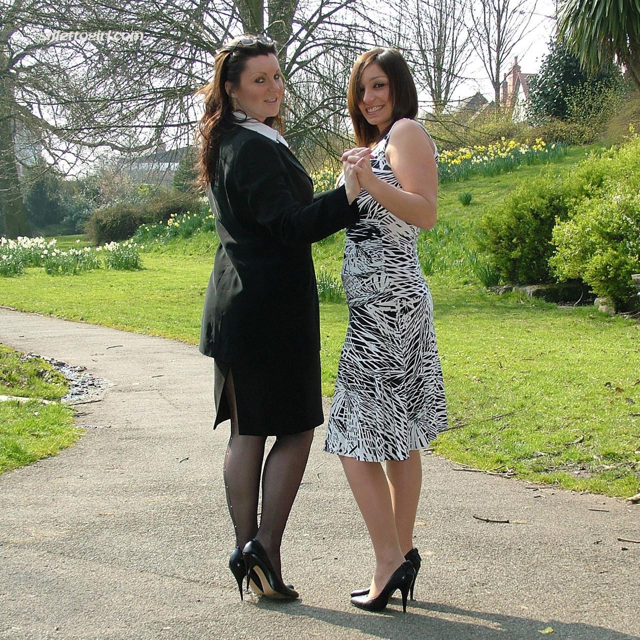 Clothed ladies hold hands while showing their spiked heels on a walking path(7)