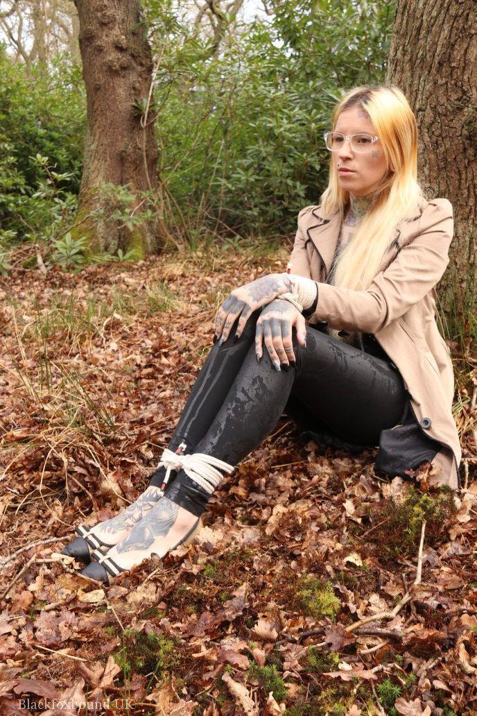 Glasses wearing woman in tied with ropes to a treed in woods with clothes on(1)