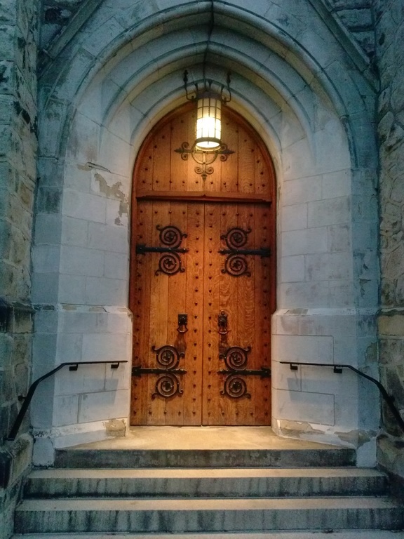 Large studded wooden door lit by lantern in gothic archway